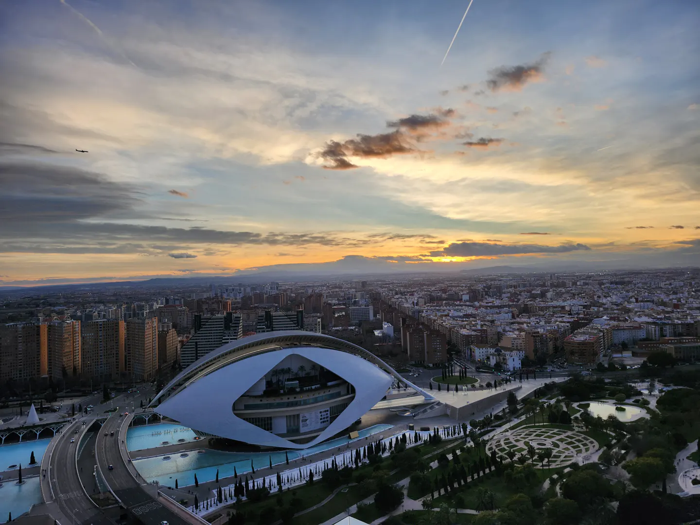 Valencia, Spain cityscape at sunset. The City of Arts and Sciences is in the foreground. Modern architecture, blue pools, and green parks.