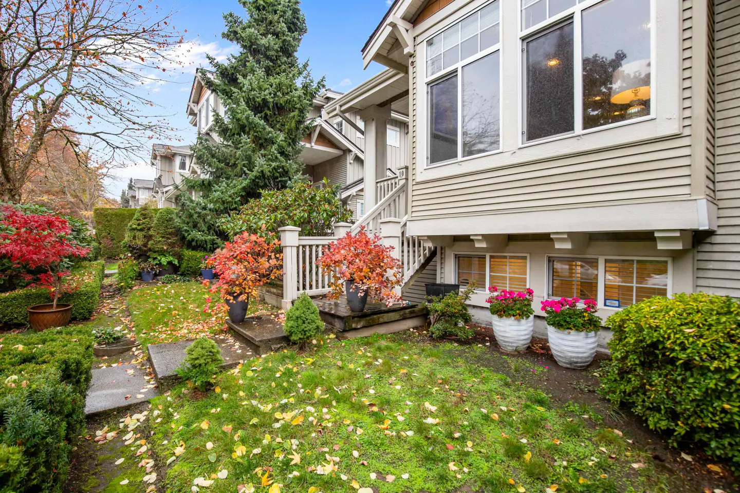 Exterior view of a beige townhouse with a well-manicured lawn, colorful foliage, and a concrete walkway.