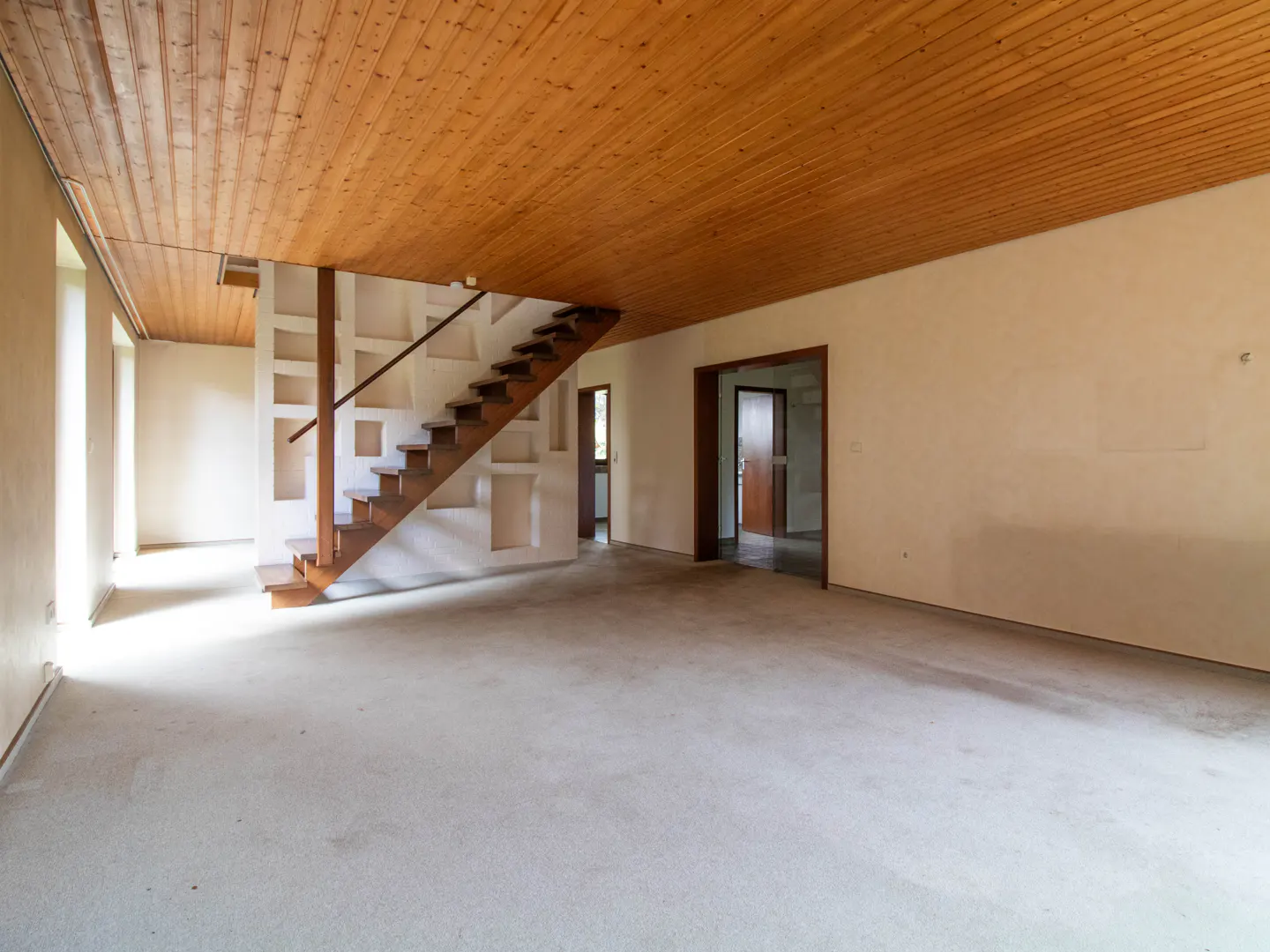 Unfurnished living room with wood ceiling, staircase with built-in shelves, and doorways leading to other rooms.