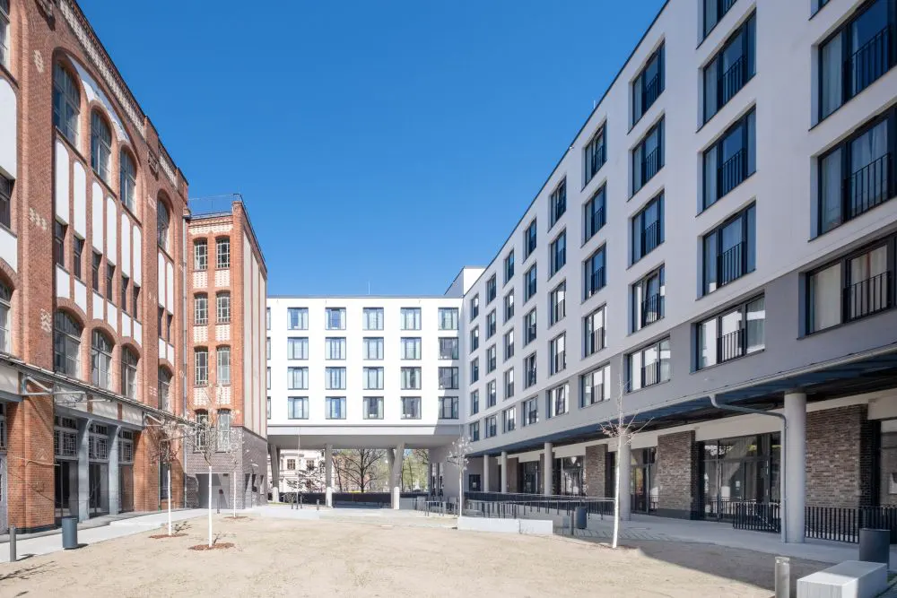 Exterior view of a courtyard surrounded by brick and white apartment buildings under a clear blue sky.