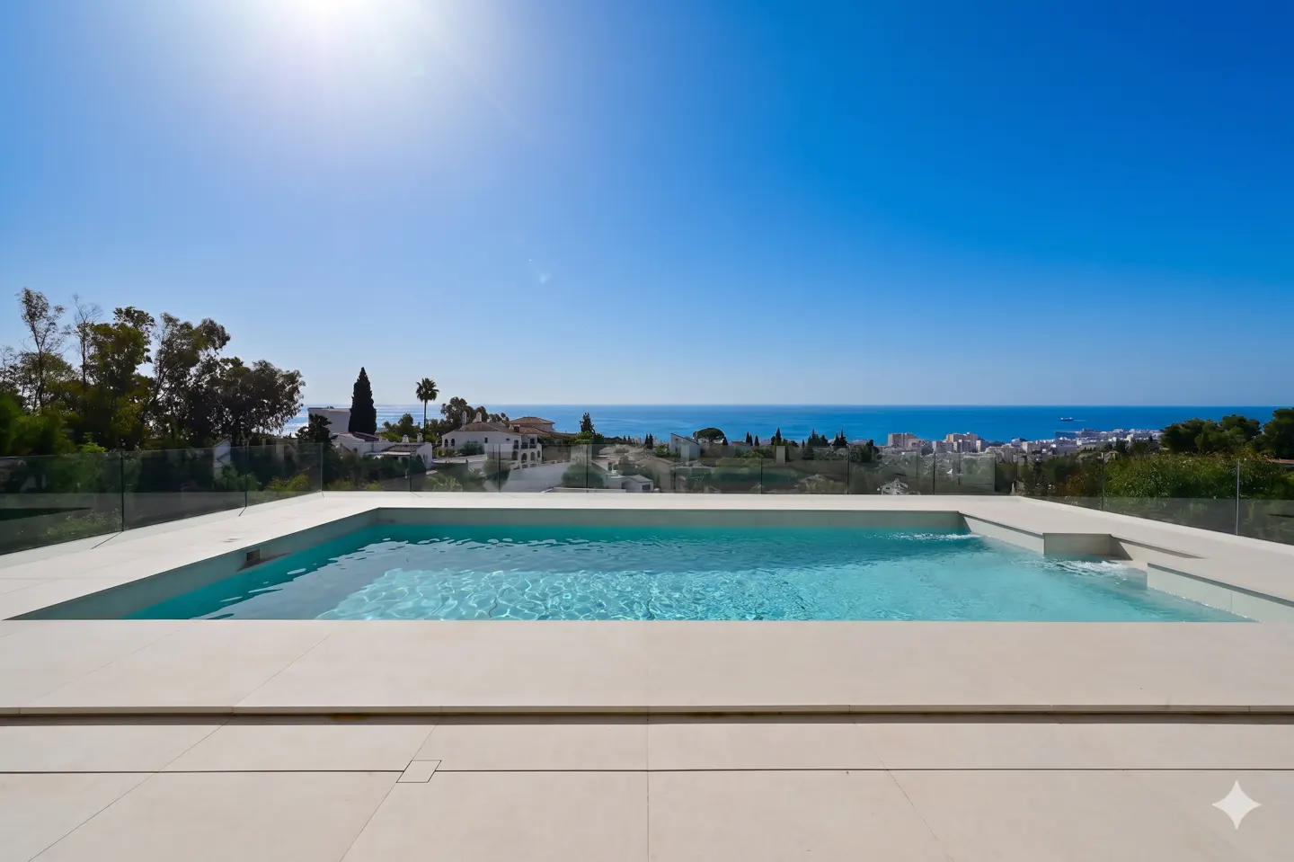 A rectangular pool with clear blue water overlooks a coastal city and the ocean under a bright blue sky.