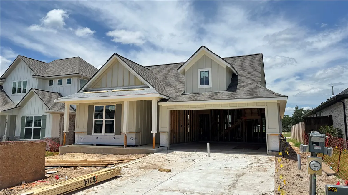 New construction home with beige siding, a gray roof, and an open garage under a blue sky with scattered clouds.