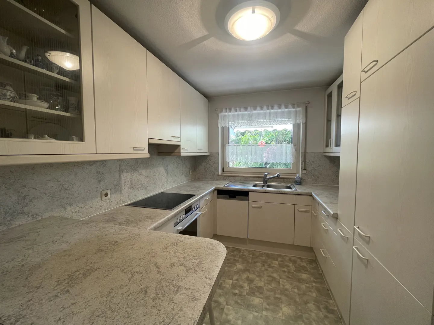 Bright kitchen with white cabinets, speckled countertops, and a window with sheer curtains. Appliances include a stove, oven, sink, and dishwasher.