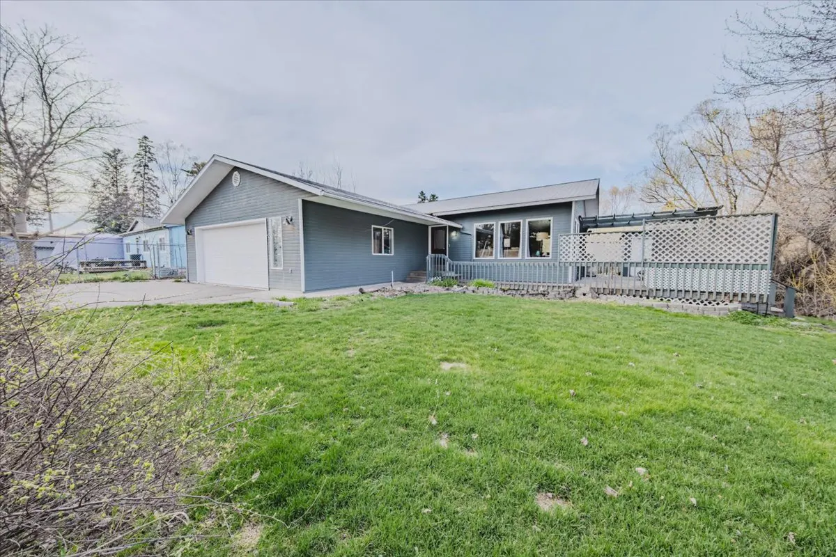 A single-story blue house with a white garage door and a green lawn. A white lattice fence surrounds a deck.