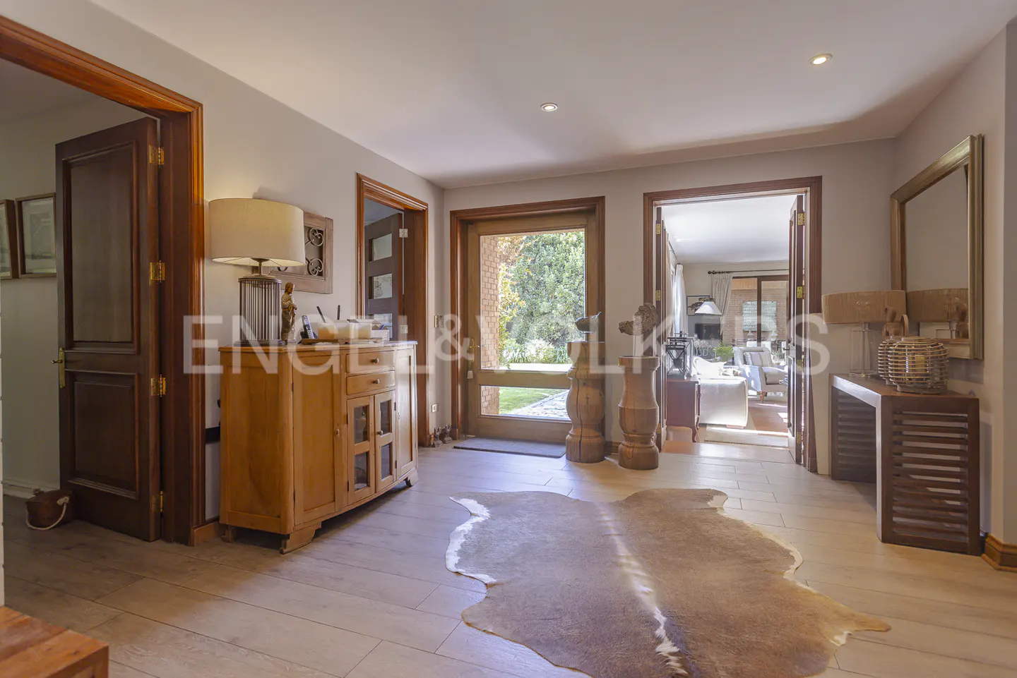 A home's foyer with wood floors, a cowhide rug, and wood furniture. A glass door leads to a green yard.