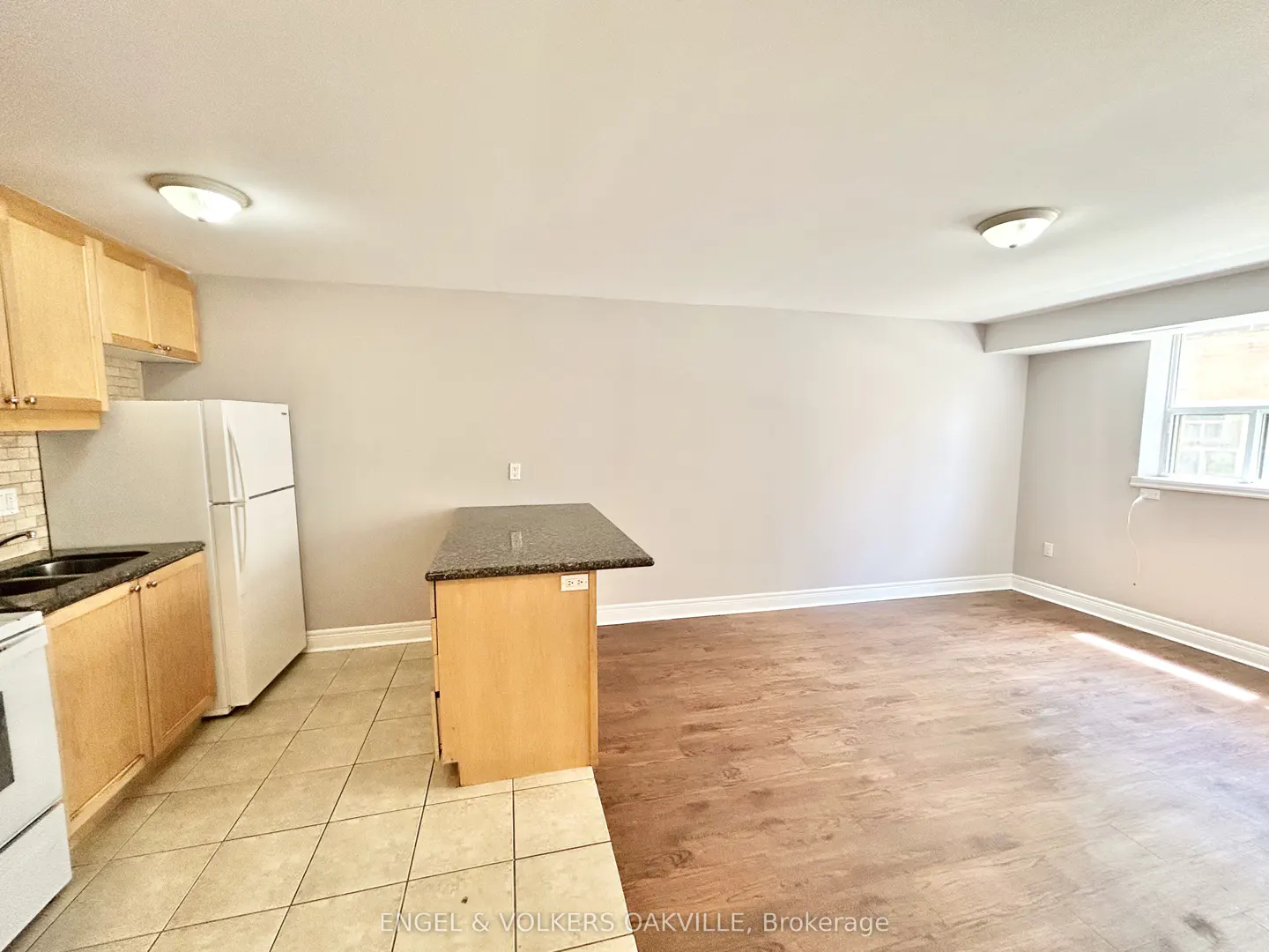 Open-concept kitchen with light wood cabinets, white appliances, a dark granite island, and wood-look flooring.