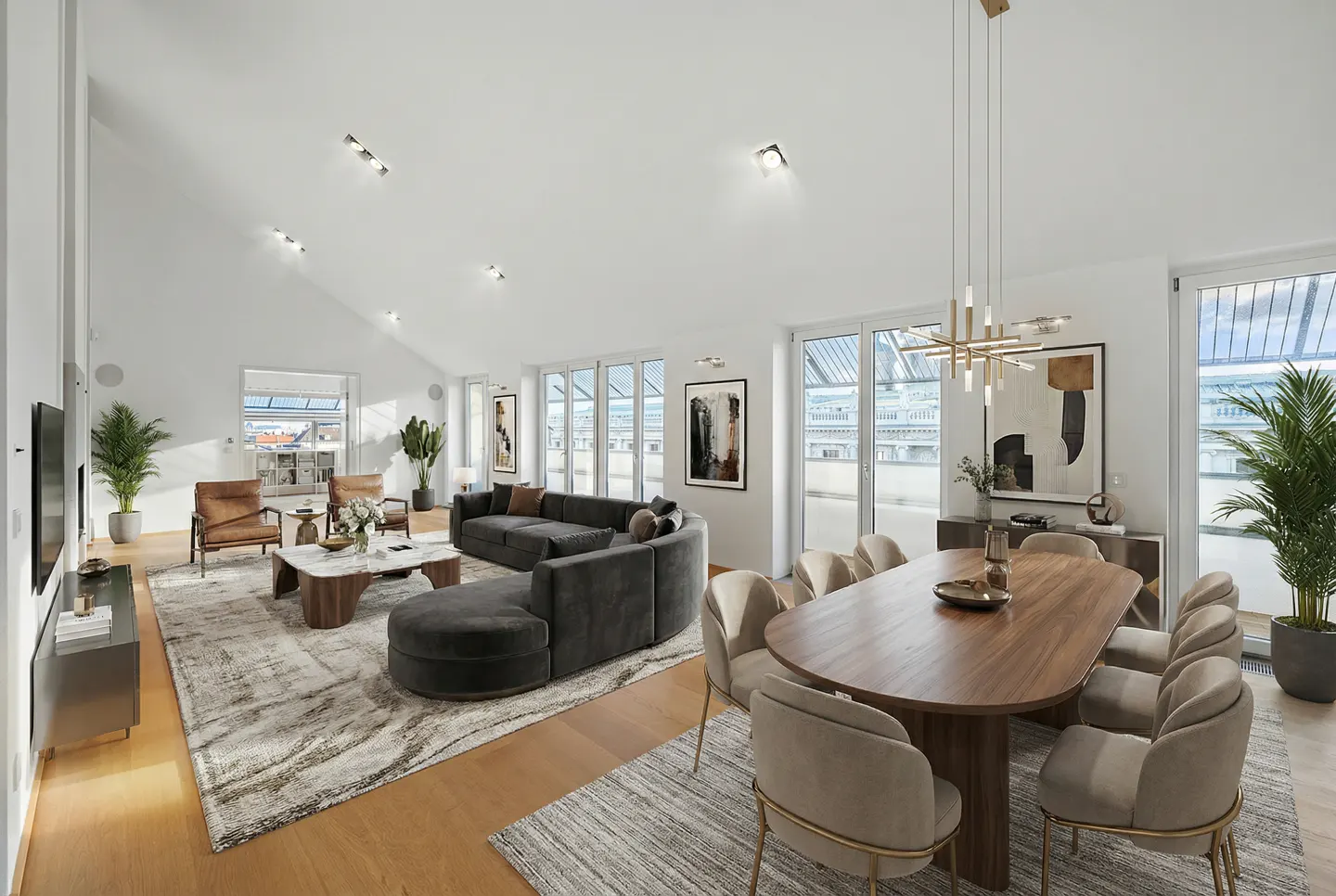 Bright, modern living and dining area with gray sofa, wood table, and large windows. Plants and artwork add to the decor.