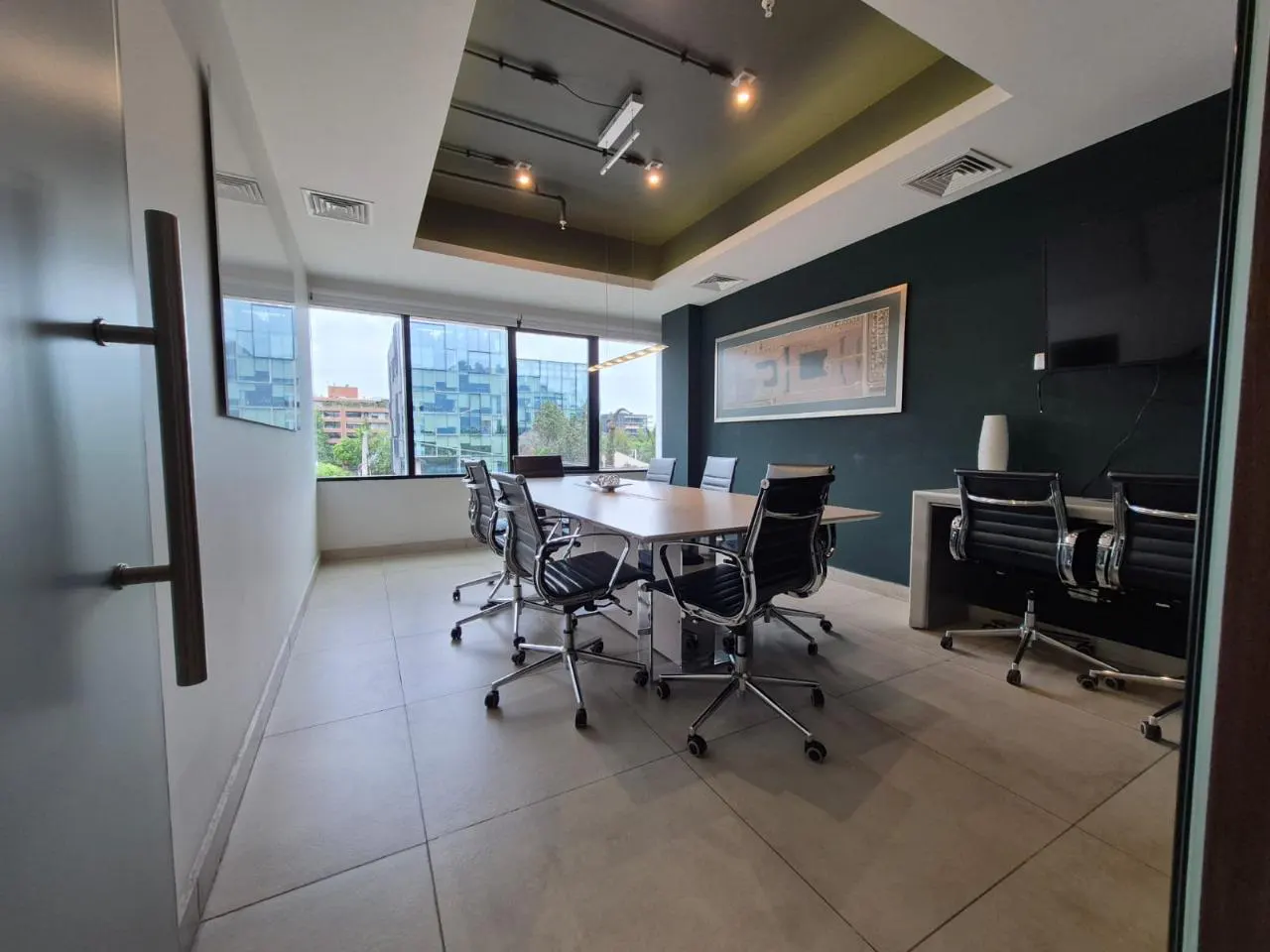 A modern conference room with a long table, black chairs, and large windows overlooking a city.