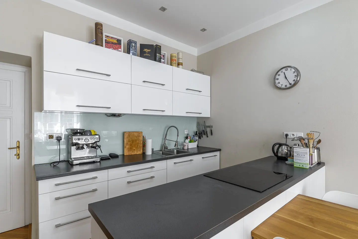 Modern kitchen with white cabinets, dark countertops, and stainless steel appliances. A clock hangs on the wall.