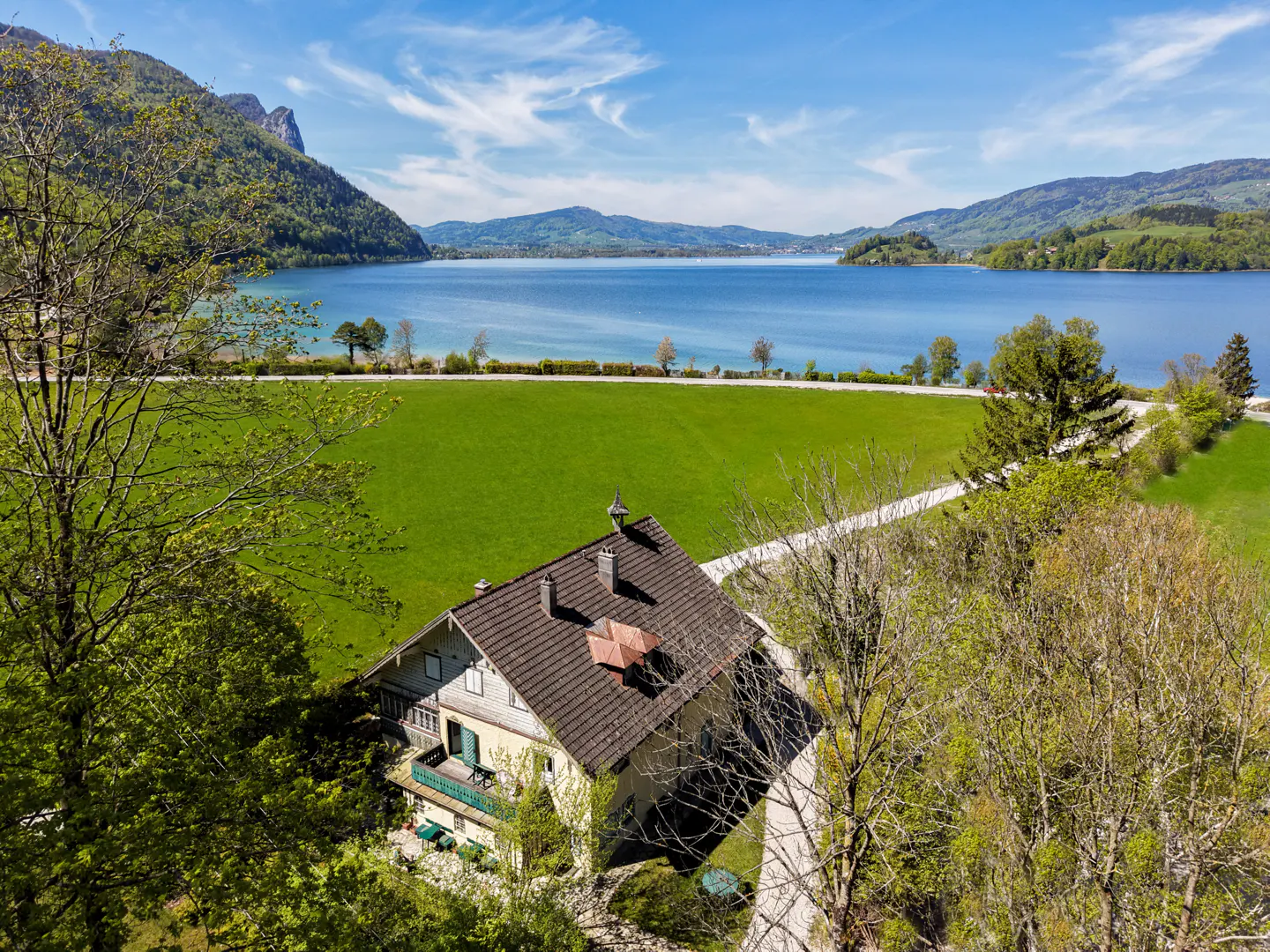 Aerial view of a yellow house with a brown roof, green lawn, and blue lake in the background.