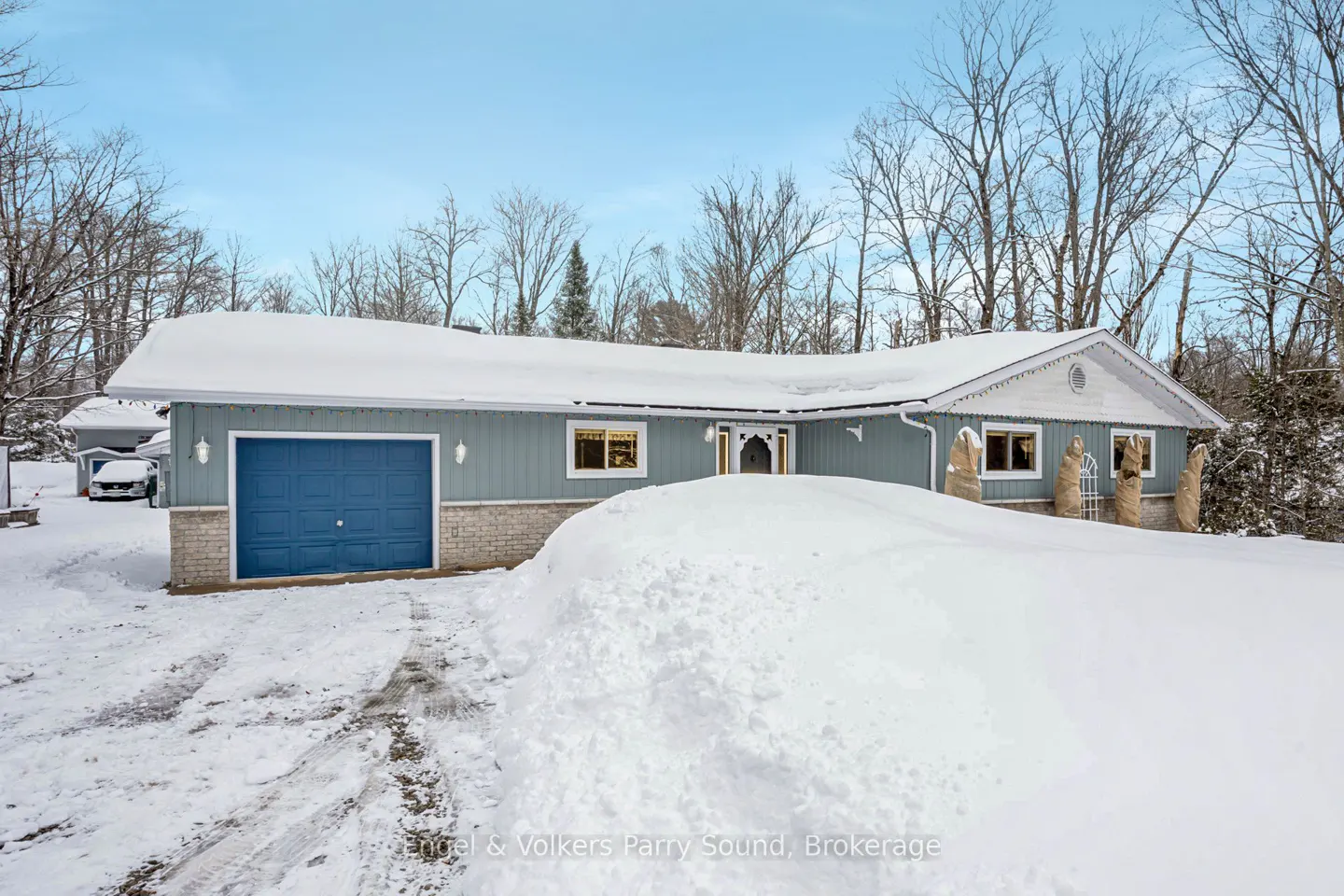 A light blue house with a blue garage door is covered in snow on a winter day.