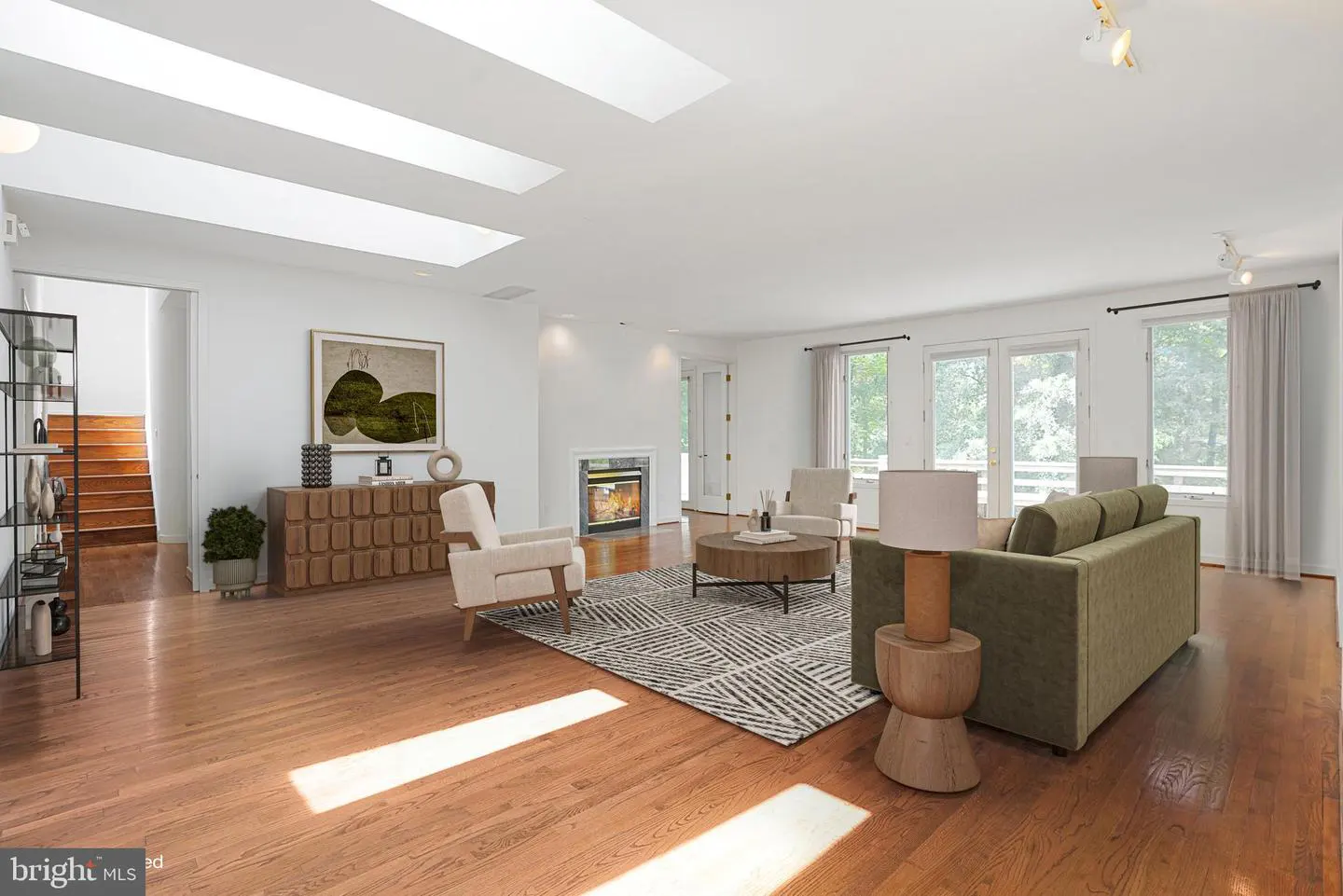 Bright, open living room with hardwood floors, skylights, and a fireplace. A green sofa and two chairs sit on a patterned rug.