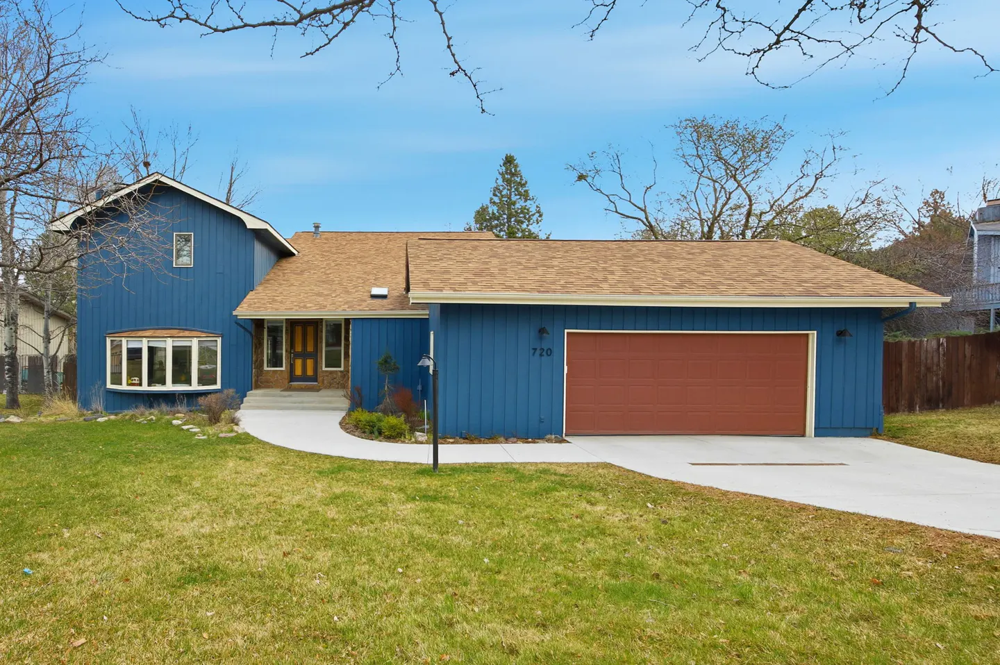 Blue two-story house with a brown roof and a brown garage door, surrounded by a green lawn and trees.