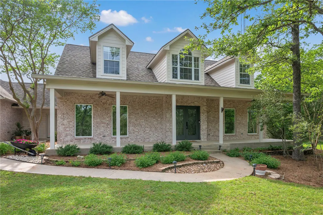 A one-story brick house with a covered porch, dormers, and a green lawn.