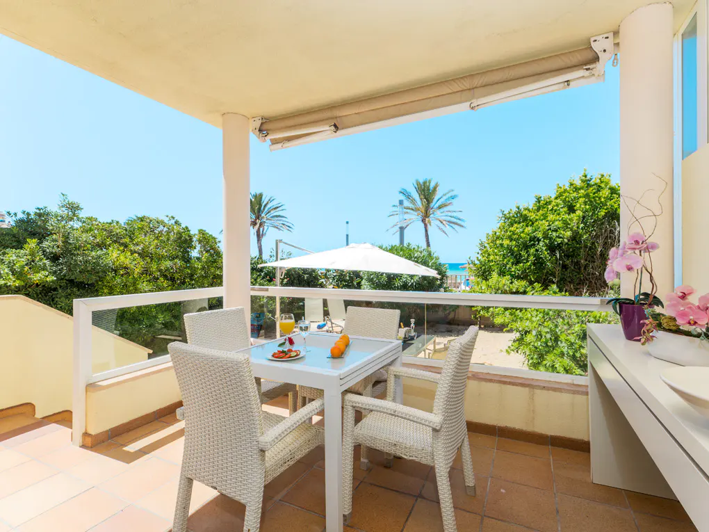 Outdoor patio with white table and chairs, set for a meal. Palm trees and beach visible in the background.