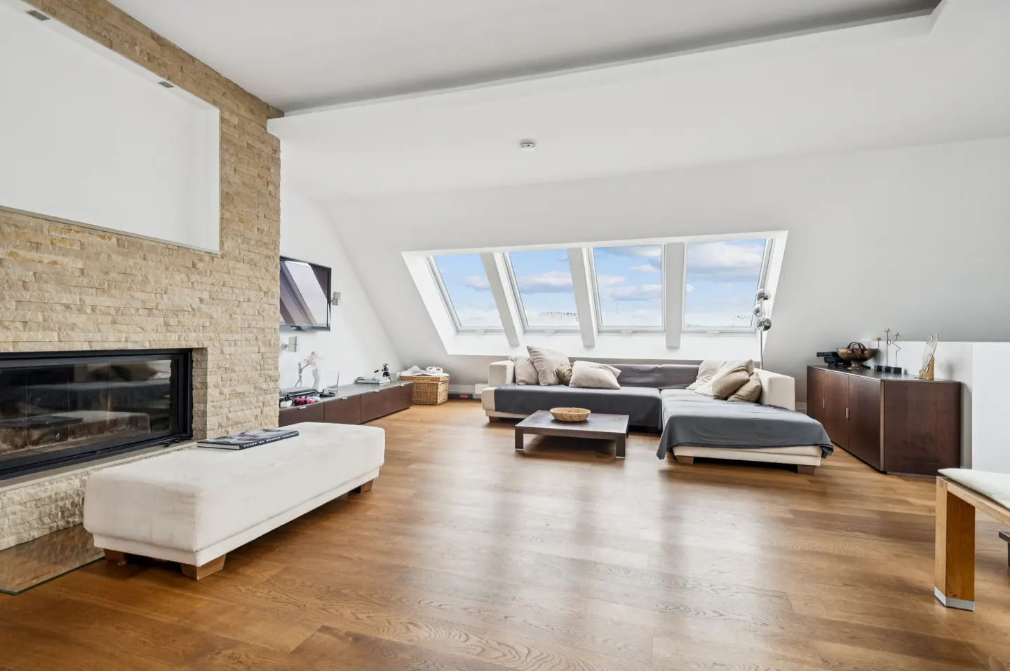 Bright living room with hardwood floors, fireplace, and skylights. A sectional sofa and ottoman provide seating.