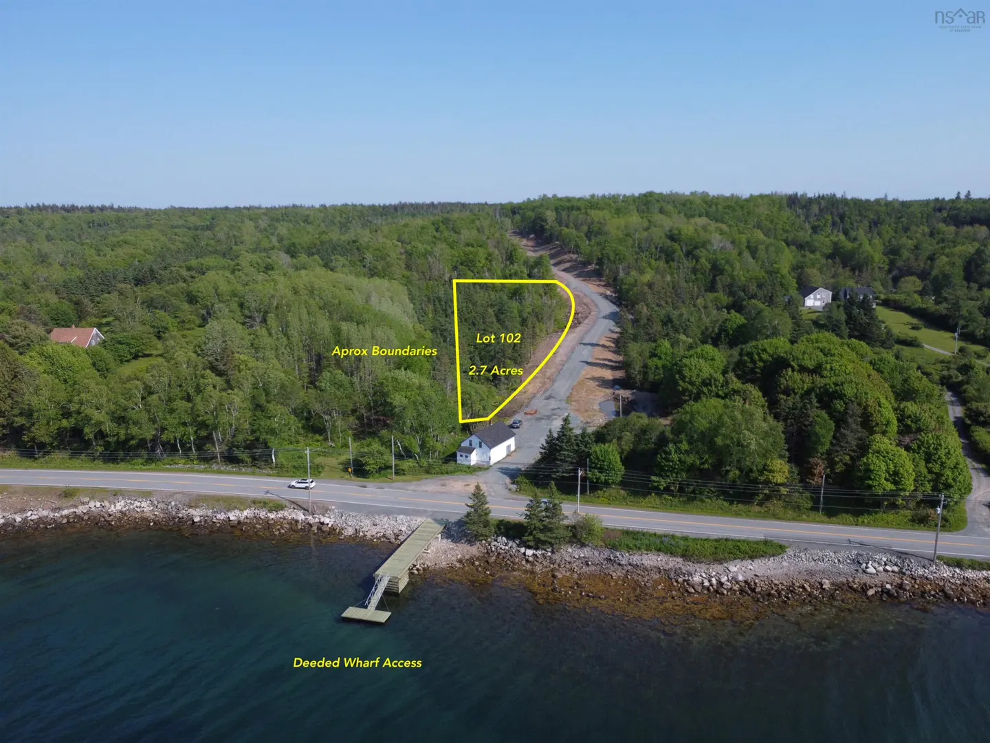 Aerial view of Lot 102, 2.7 acres, with yellow boundary lines, near a road, wharf, and ocean. Forest background.