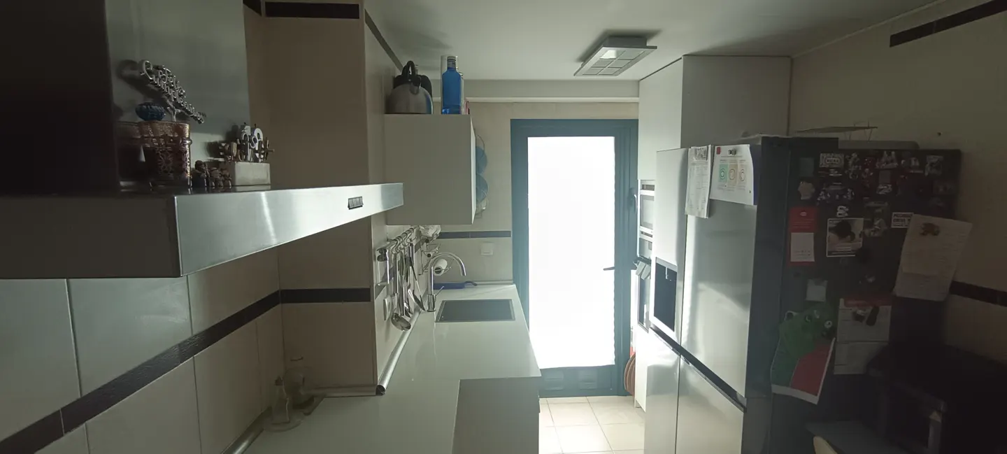 A narrow kitchen with white cabinets, stainless steel appliances, and a bright window at the end.