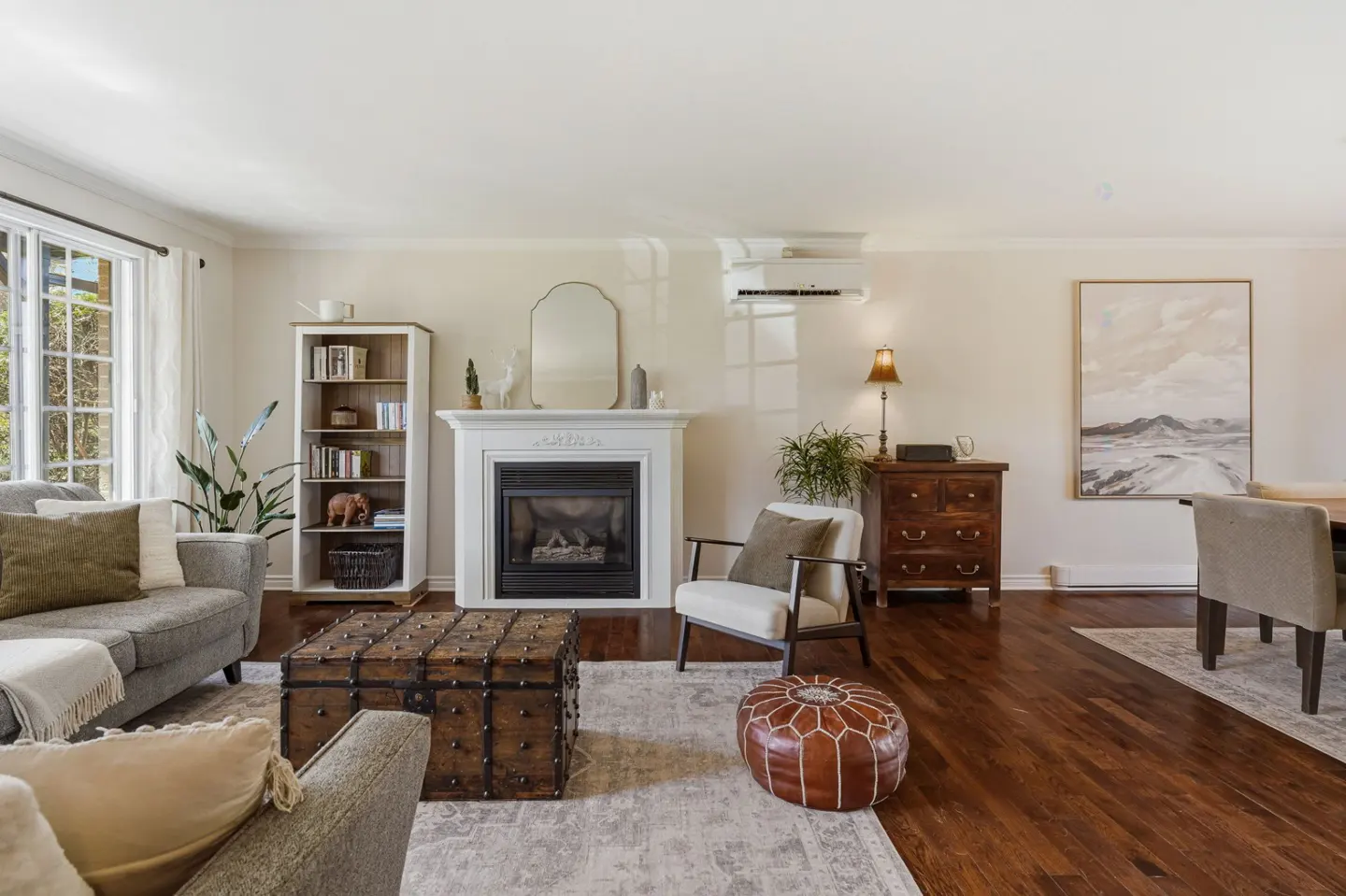 Living room with a gray sofa, white fireplace, and a wooden chest coffee table on a patterned rug.