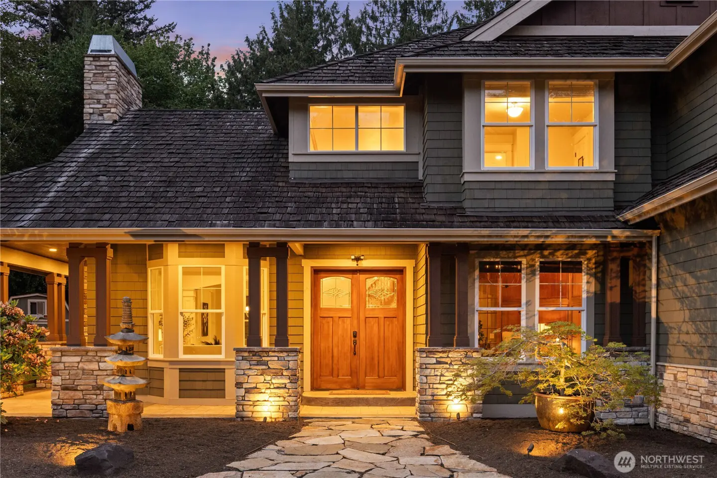 Exterior of a two-story home with a stone walkway leading to a wood front door. Windows glow with warm light.