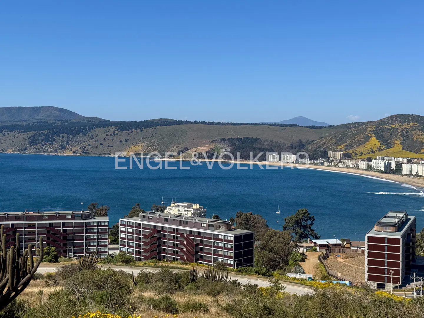 Scenic view of coastal apartments overlooking a blue bay, with mountains in the background under a clear sky.