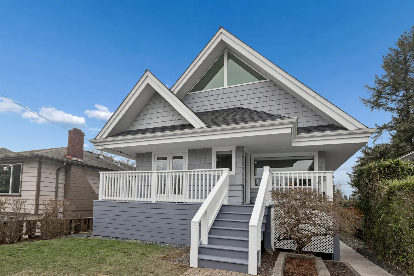 Exterior of a gray house with a white porch and stairs under a blue sky.