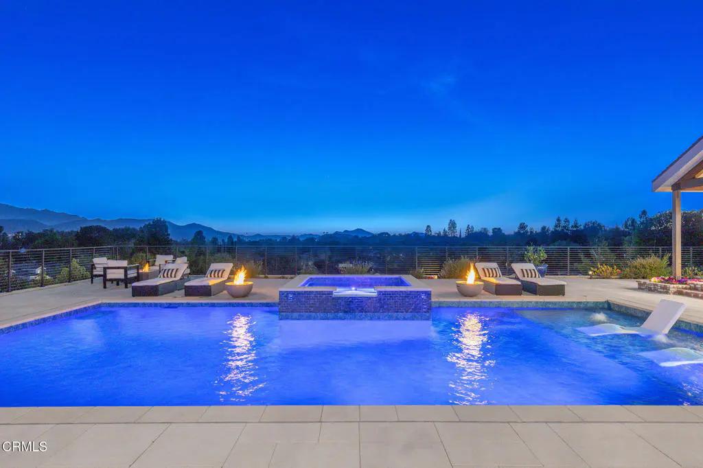 Luxury pool and spa at twilight with fire bowls, lounge chairs, and a scenic mountain view in the background.