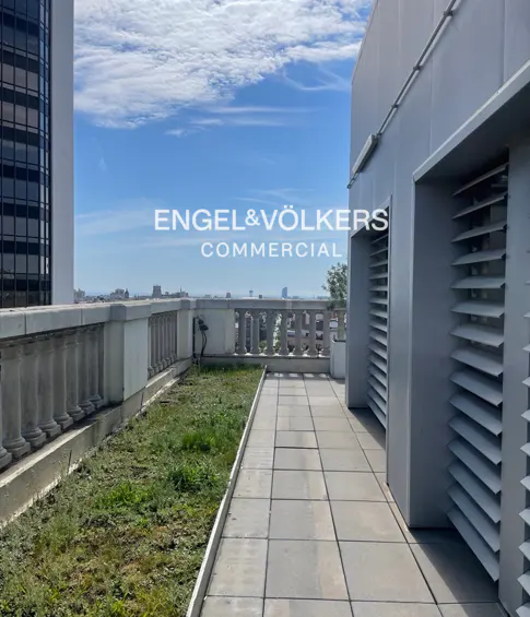Engel & Völkers commercial property with a rooftop terrace, stone balustrade, green grass, and city views under a blue sky.