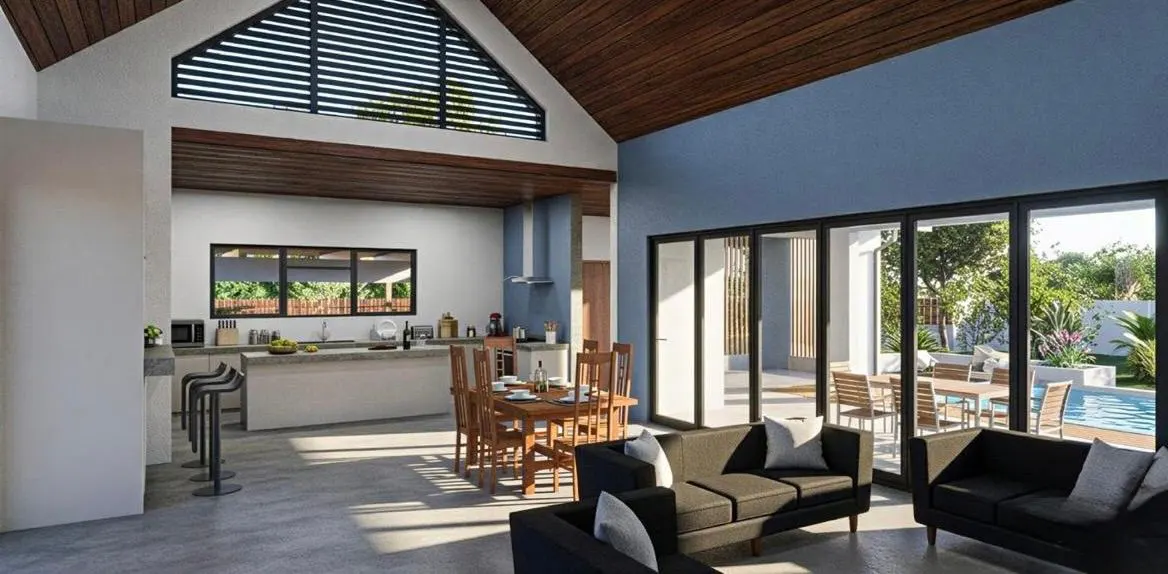 Open-plan living area with vaulted wood ceiling, modern kitchen, dining set, and black sofas facing a pool patio.
