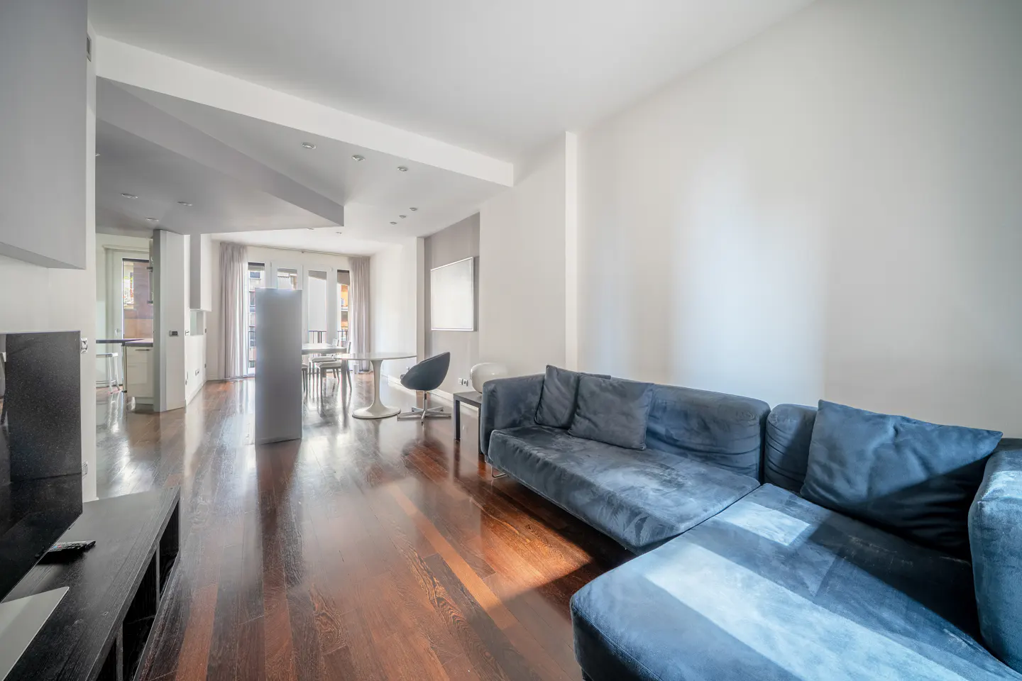 Bright living room with hardwood floors, a blue sectional sofa, and a dining area with a round table and chairs.