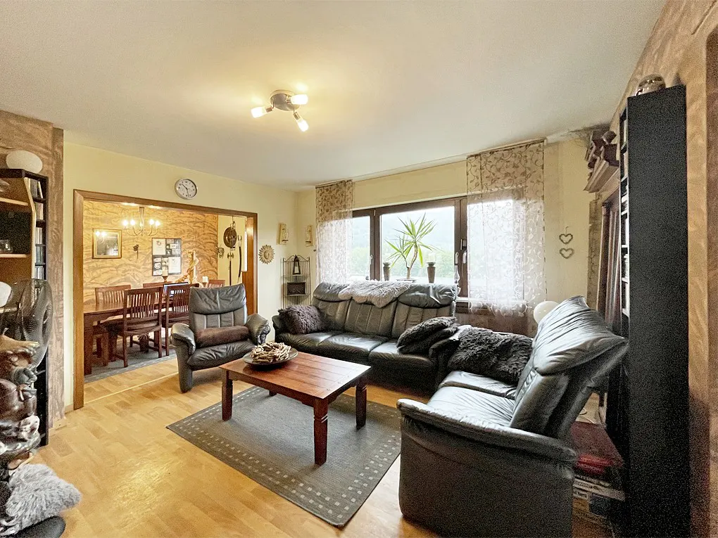 Living room with black leather sofas, wood floors, and a dining room visible through an archway. A brown coffee table sits on a gray rug.