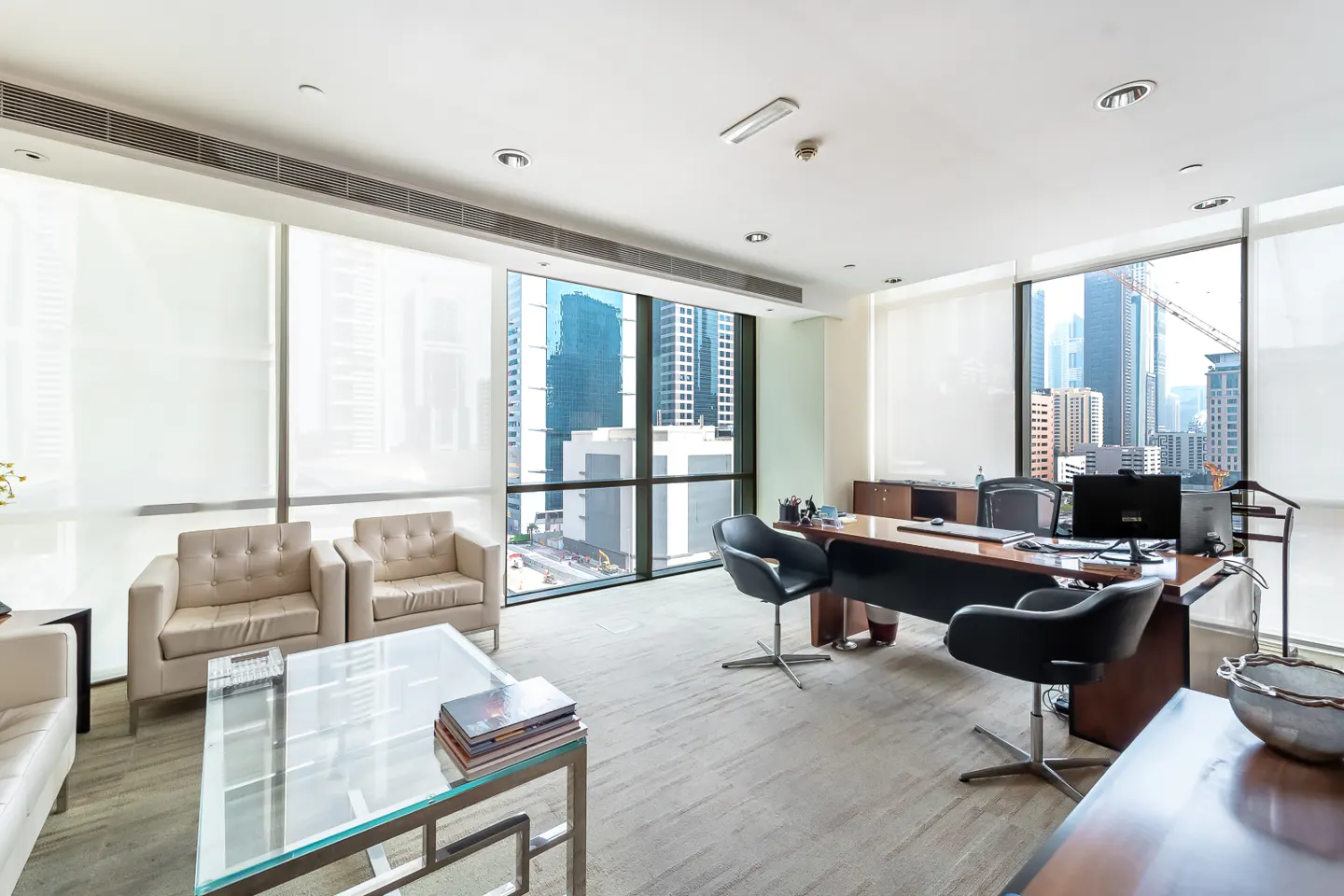 Bright office space with a large window overlooking a city. There are chairs, a desk, and a glass table in the room.