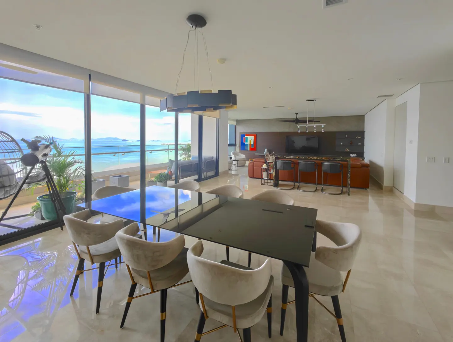Open-concept living space with a black dining table, beige chairs, and ocean view through large windows.