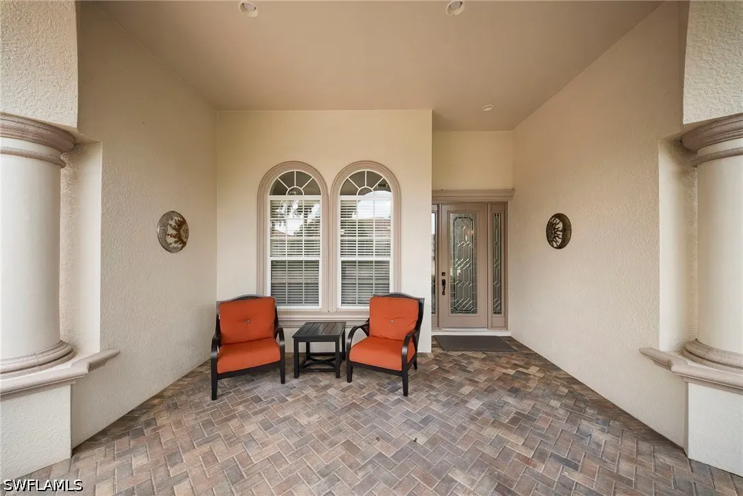 Covered porch with brick floor, two orange chairs, a small table, and a front door with decorative glass.