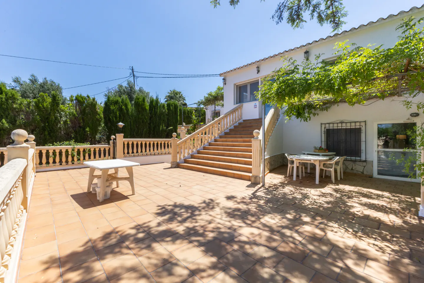 Exterior view of a white house with a tiled patio, stairs leading to the entrance, and outdoor furniture.