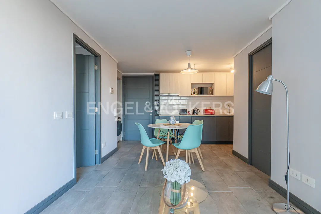Modern open-plan apartment with a dining area, light blue chairs, and a kitchen with two-tone cabinets and grey floors.
