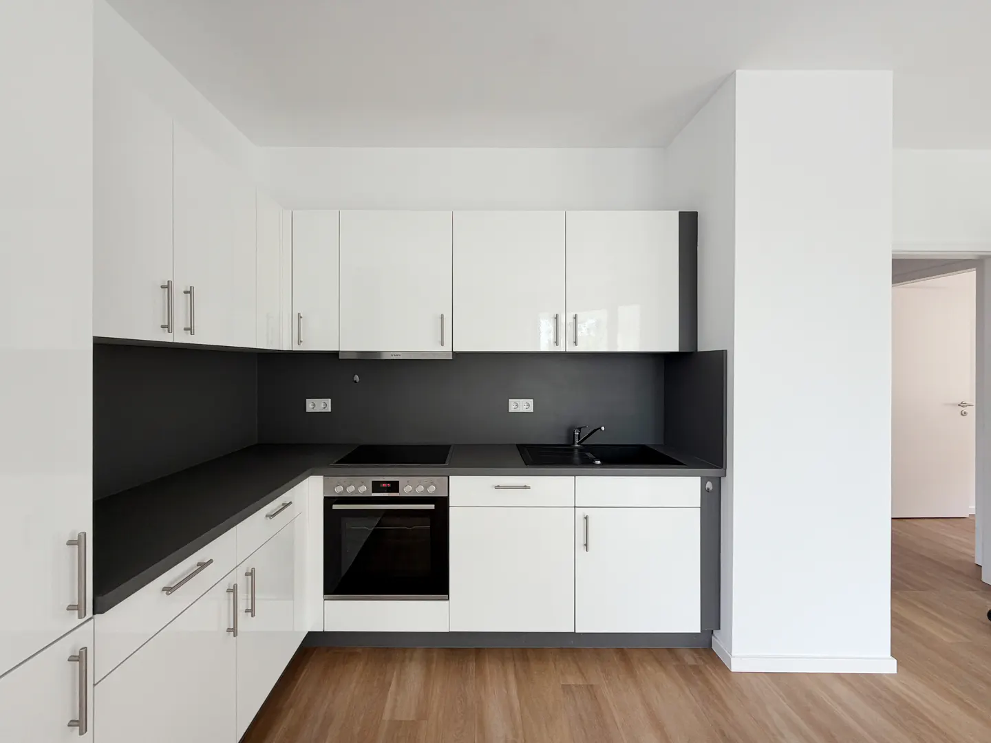 Bright kitchen with white cabinets, gray countertops and backsplash, stainless steel appliances, and wood-look flooring.