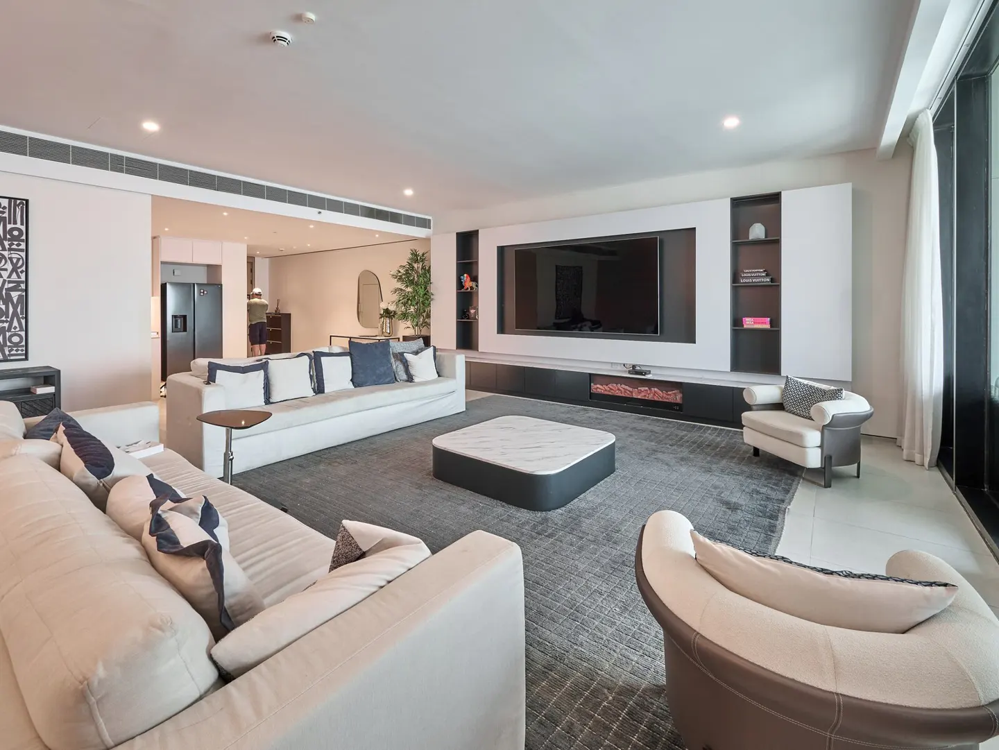 A modern living room with white sofas, a gray rug, and a large TV.