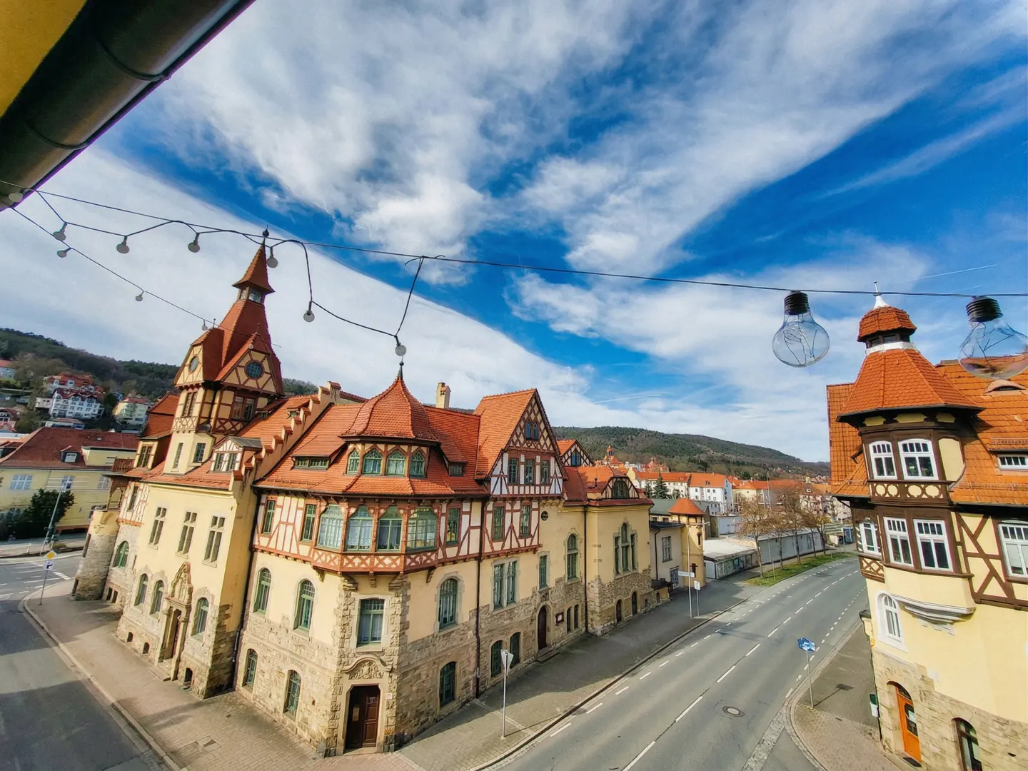 View of historic half-timbered buildings with orange roofs and stone bases along a quiet street under a blue sky.