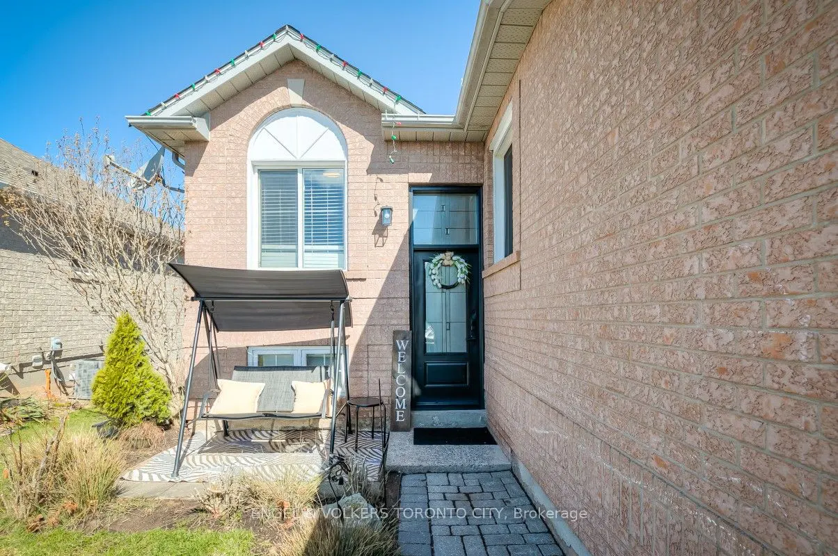 Exterior view of a brick house with a black front door, a "Welcome" sign, and a porch swing.