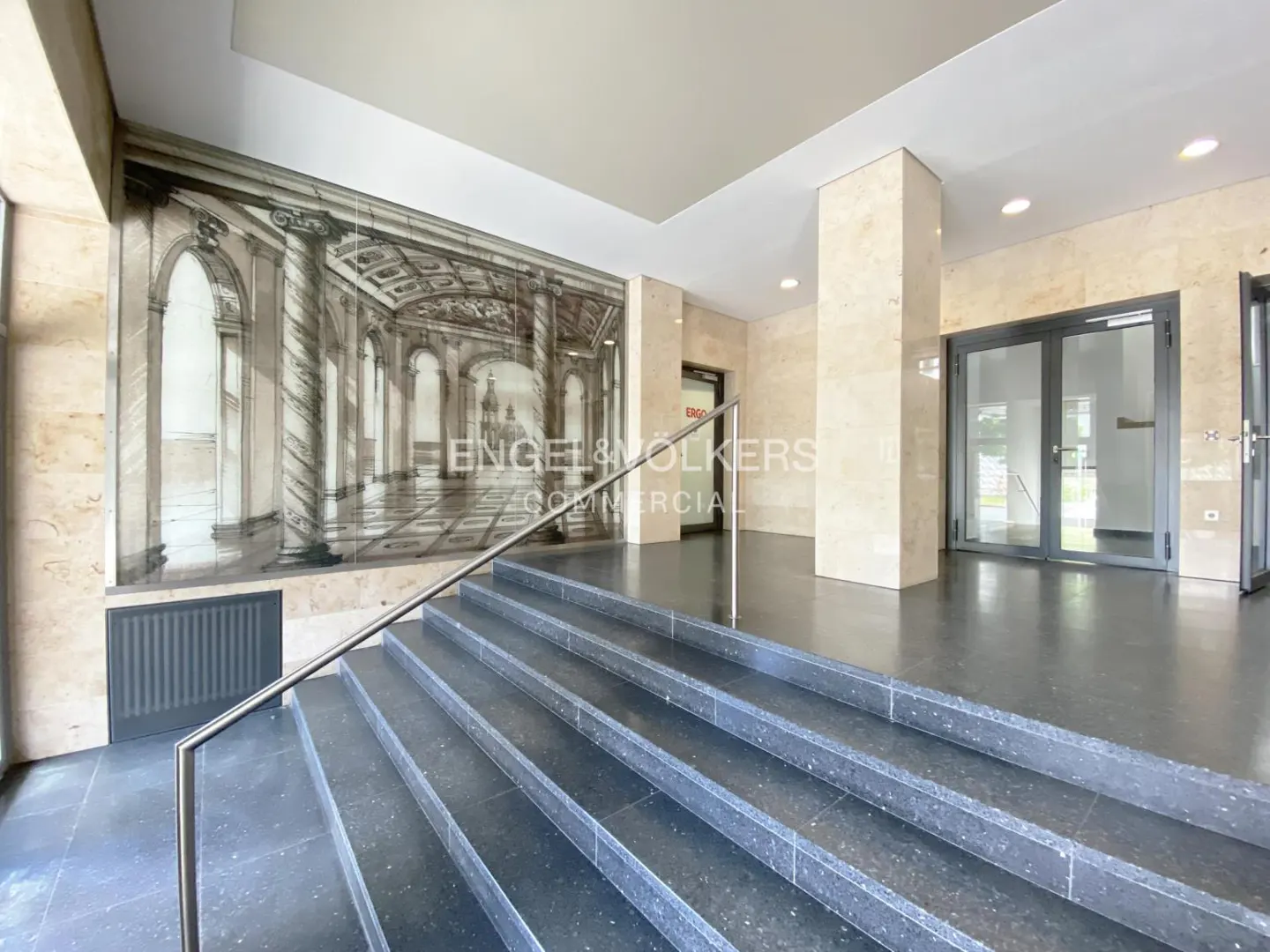 Interior view of a commercial building lobby with black stairs, marble walls, and a large mural.