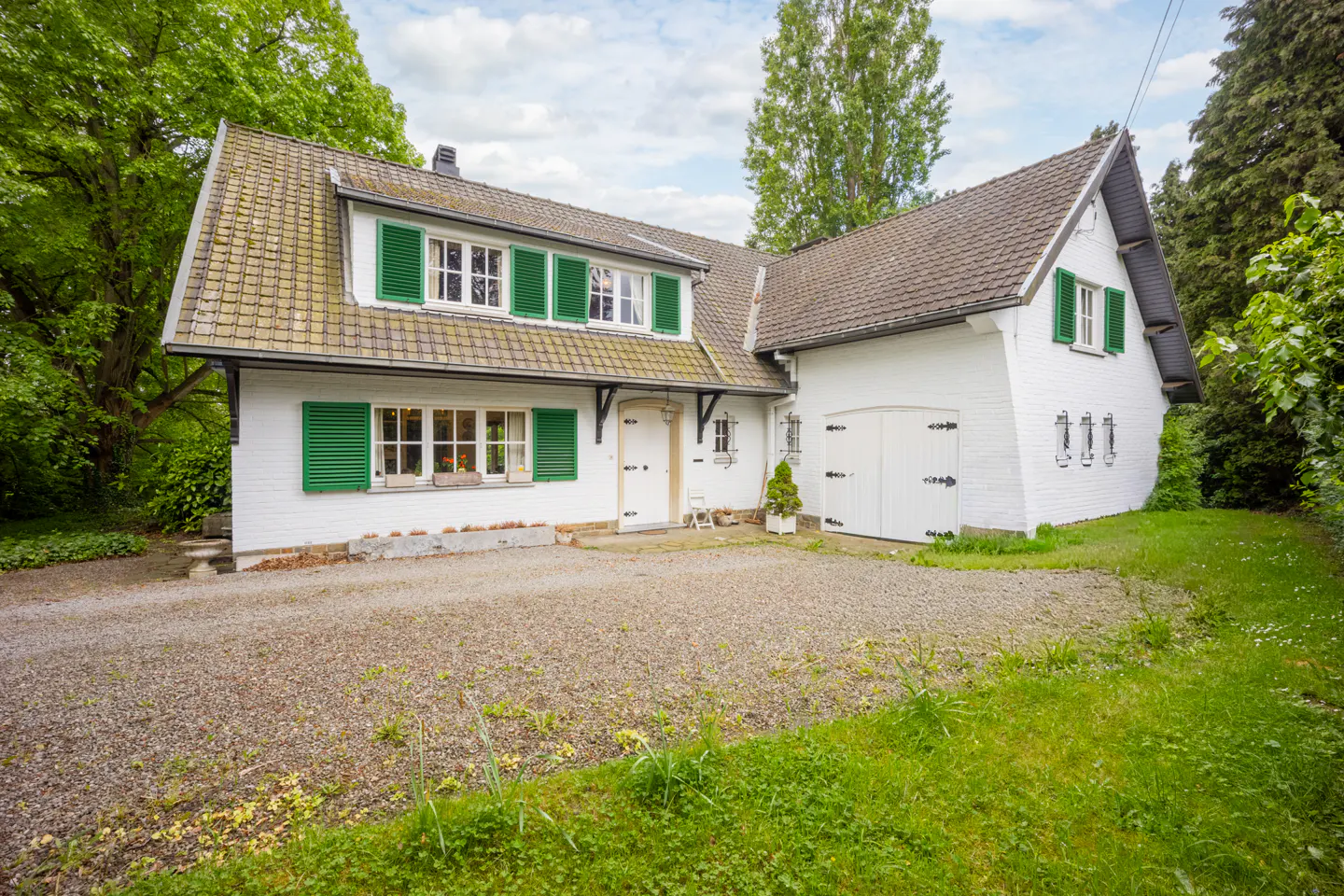 Exterior view of a white house with green shutters and a gravel driveway.