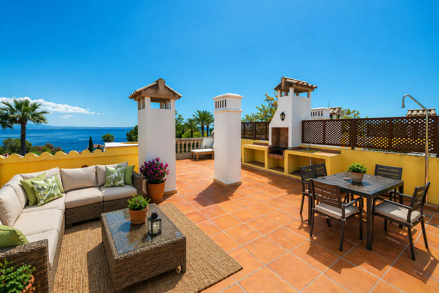 Outdoor rooftop patio with a beige sectional sofa, a table, and a dining set with a grill, under a clear blue sky.