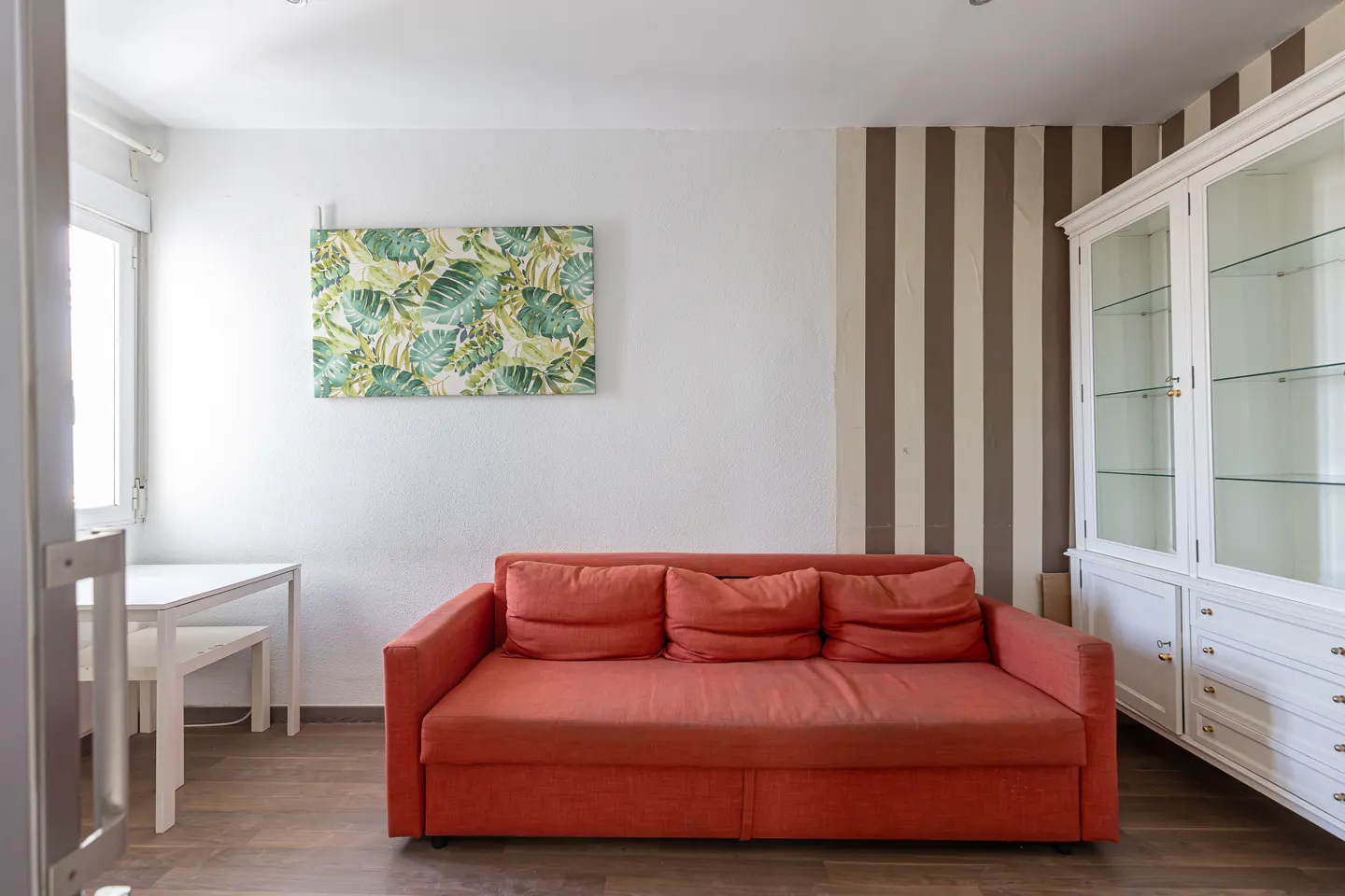 Living room with an orange sofa, white table and cabinet, and a tropical-themed painting.