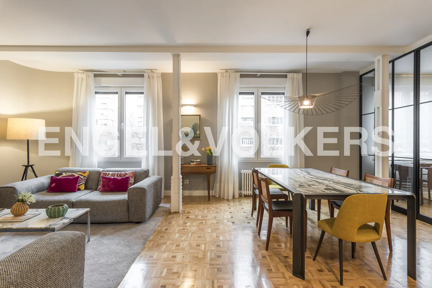 Modern living room with a grey sofa, marble dining table, yellow chairs, and parquet flooring in a bright, open space.