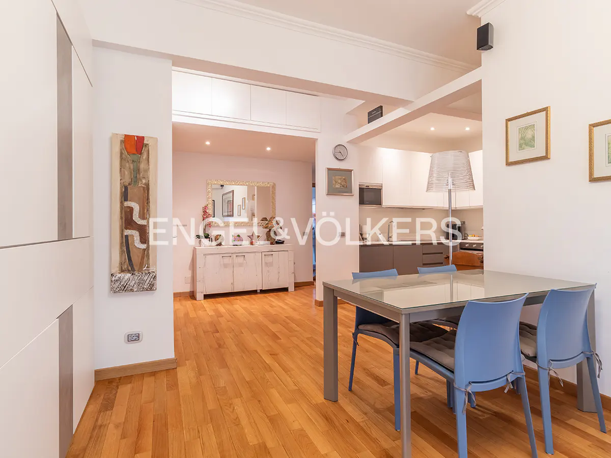 Open-concept living space with hardwood floors, a dining table with blue chairs, and a view into the kitchen and living room.