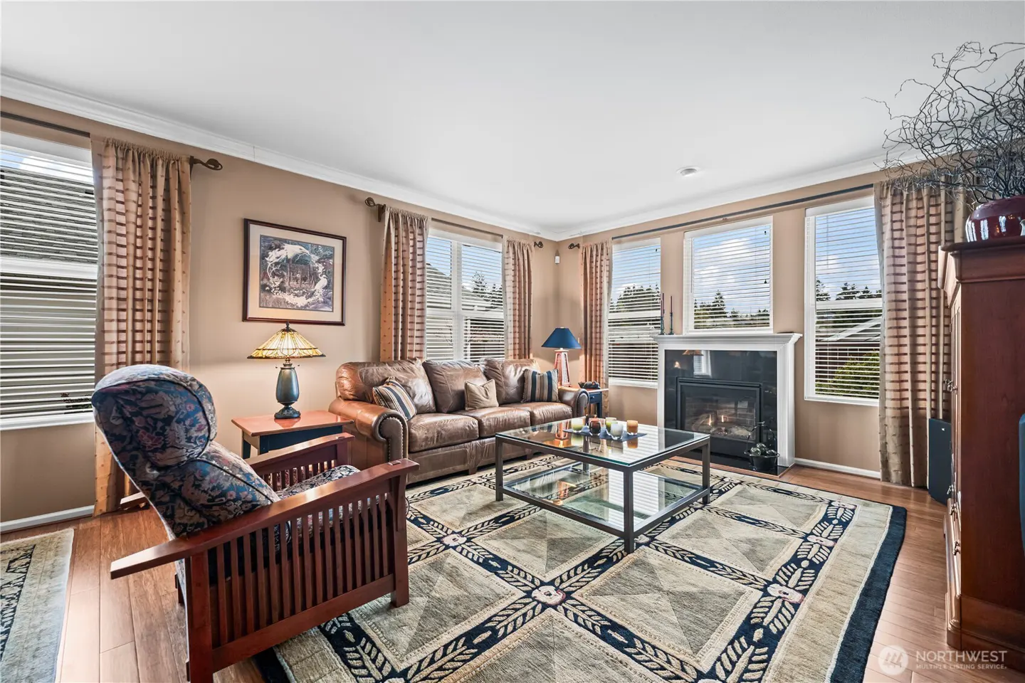 Living room with brown leather sofa, patterned chair, glass coffee table, fireplace, and large patterned rug.