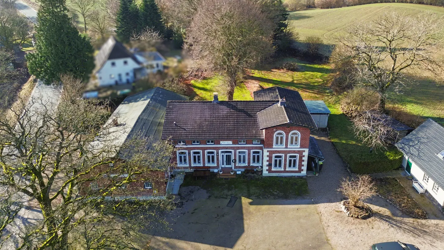 Aerial view of a red brick house with a dark roof, surrounded by trees and greenery.