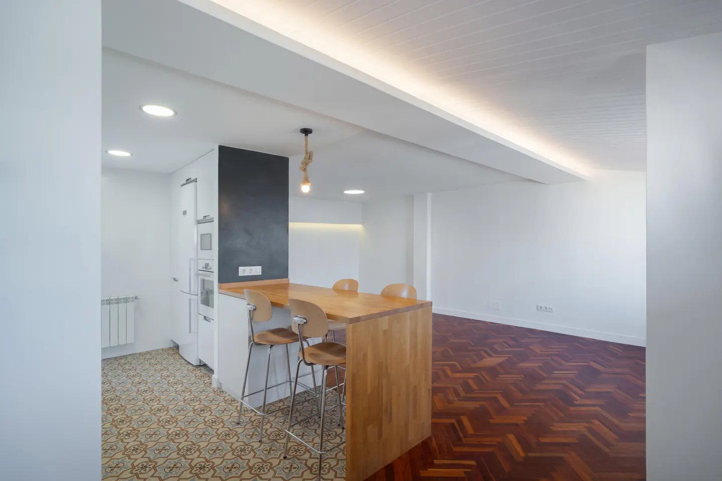 Bright, modern kitchen with a wooden island and bar stools. White walls and cabinets contrast with the dark backsplash and herringbone wood floors.