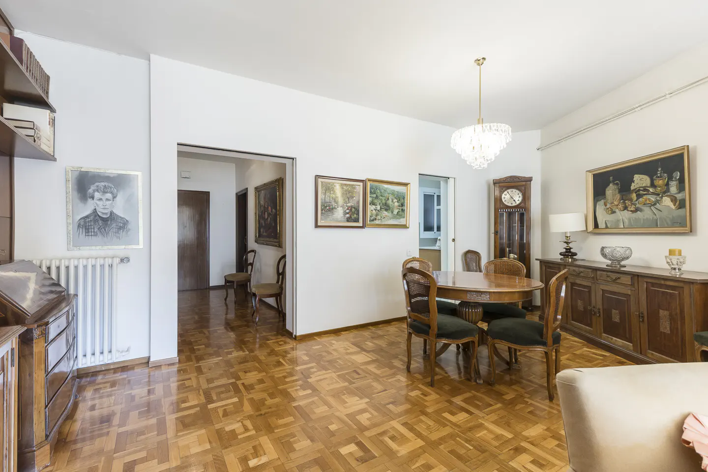 A bright dining room with parquet floors, a round wooden table with green chairs, and antique furniture.